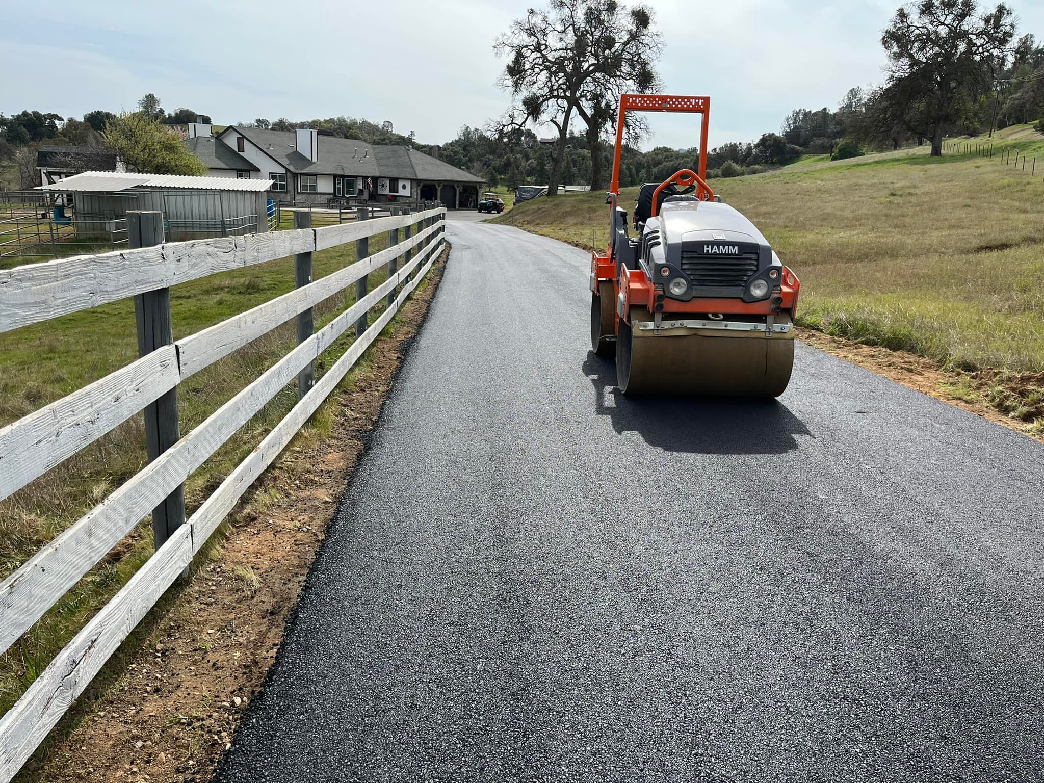 Roller compacting fresh asphalt on rural road with fence in Michigan