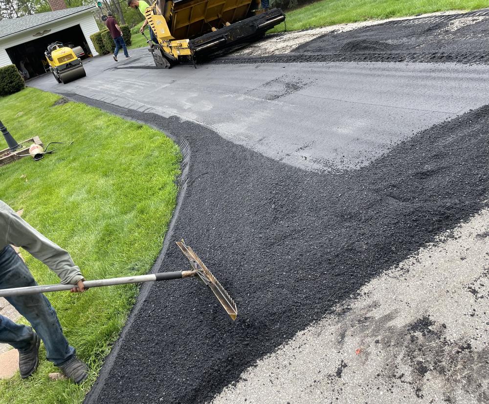 Crew raking fresh asphalt on residential driveway